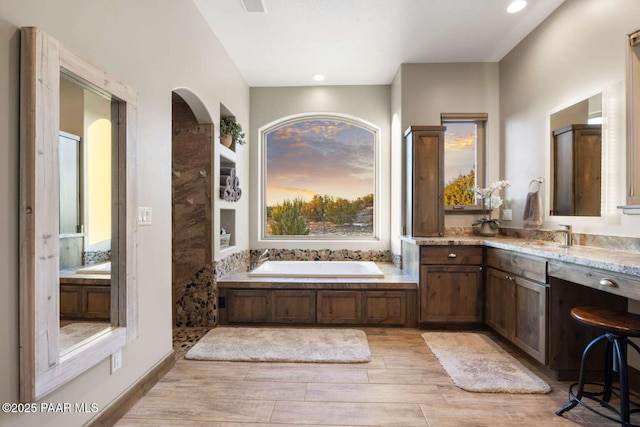 bathroom featuring wood finish floors, a garden tub, recessed lighting, and vanity