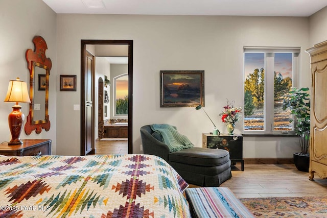 bedroom with arched walkways, connected bathroom, baseboards, and wood finished floors