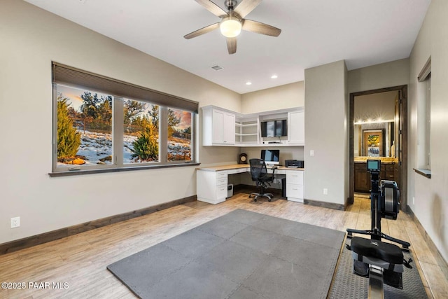 office area featuring light wood finished floors, visible vents, baseboards, built in desk, and a ceiling fan