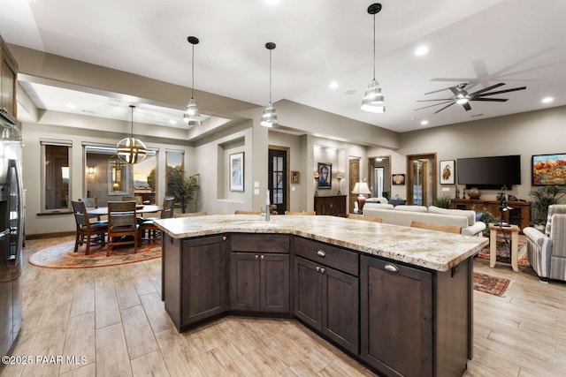 kitchen featuring light wood-type flooring, recessed lighting, hanging light fixtures, dark brown cabinets, and open floor plan