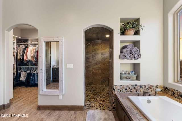 full bath featuring a garden tub, a spacious closet, wood finished floors, and tiled shower