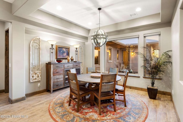 dining area with a tray ceiling, visible vents, baseboards, and light wood-style flooring