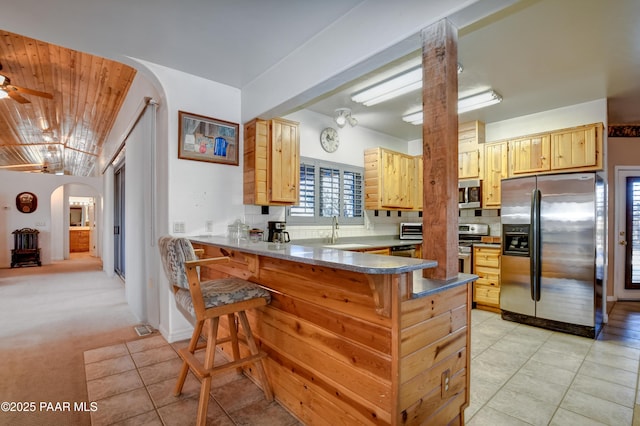 kitchen with kitchen peninsula, appliances with stainless steel finishes, light colored carpet, and light brown cabinetry