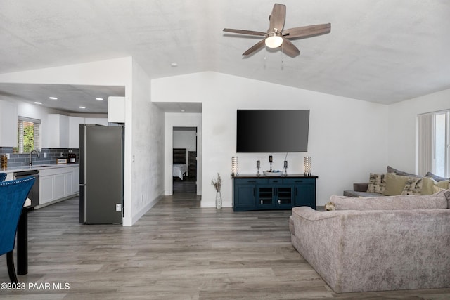 living room featuring ceiling fan, sink, vaulted ceiling, and light wood-type flooring