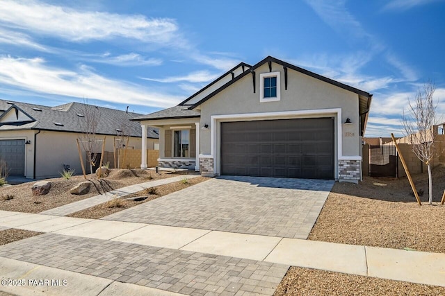 view of front facade with stone siding, an attached garage, fence, decorative driveway, and stucco siding