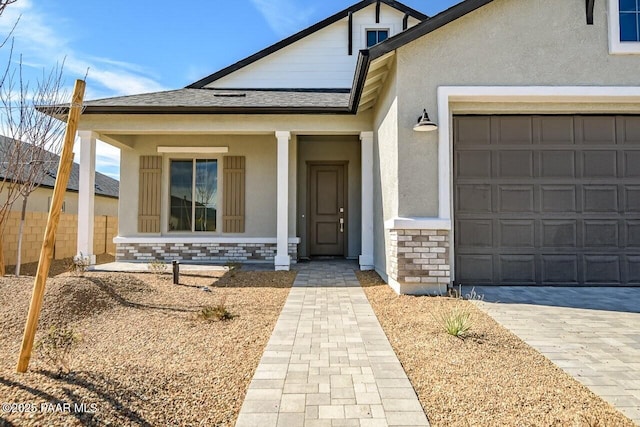 entrance to property featuring stucco siding, a shingled roof, decorative driveway, and brick siding