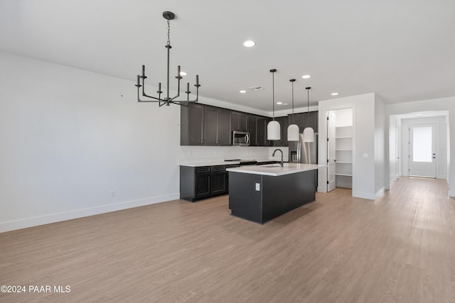 kitchen with sink, light hardwood / wood-style flooring, a chandelier, hanging light fixtures, and an island with sink