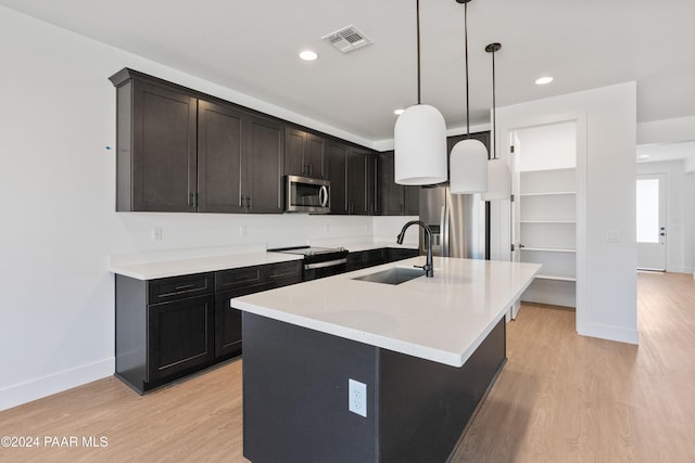 kitchen with sink, light hardwood / wood-style flooring, decorative light fixtures, a center island with sink, and appliances with stainless steel finishes