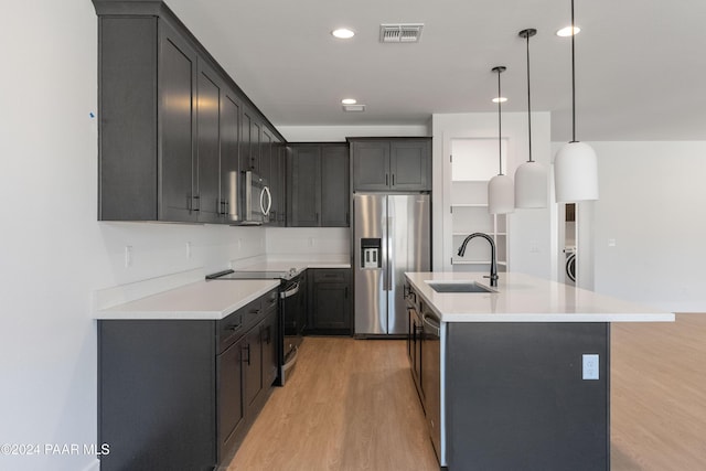 kitchen with sink, hanging light fixtures, light hardwood / wood-style floors, a kitchen island with sink, and appliances with stainless steel finishes