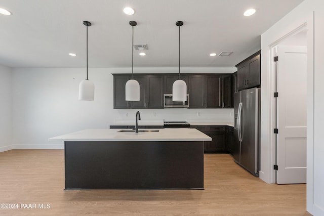 kitchen featuring appliances with stainless steel finishes, light wood-type flooring, sink, hanging light fixtures, and an island with sink