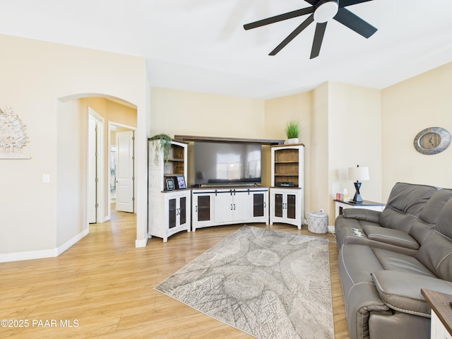living area with arched walkways, wood finished floors, baseboards, and ceiling fan