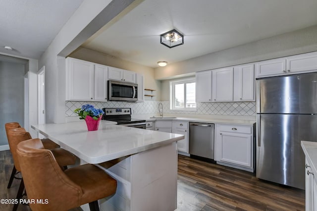 kitchen featuring dark wood finished floors, a peninsula, a sink, white cabinets, and appliances with stainless steel finishes