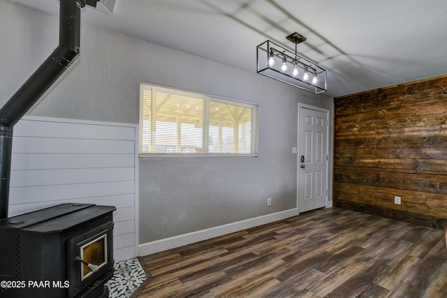 unfurnished dining area featuring baseboards, dark wood-type flooring, wood walls, and a wood stove