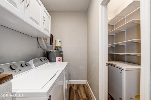 laundry room featuring electric water heater, baseboards, dark wood finished floors, washing machine and dryer, and cabinet space