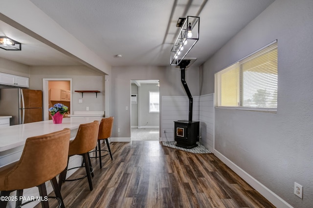 dining space with track lighting, a textured ceiling, dark wood-style floors, baseboards, and a wood stove