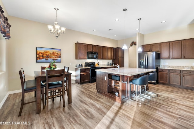 kitchen featuring black appliances, sink, hanging light fixtures, light stone countertops, and an island with sink