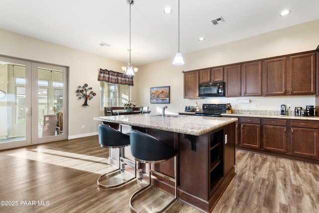 kitchen with pendant lighting, a kitchen island with sink, black appliances, hardwood / wood-style flooring, and light stone counters