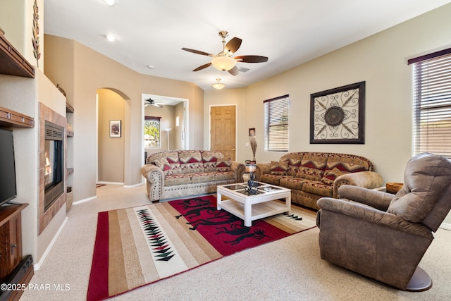 living room featuring arched walkways, baseboards, a ceiling fan, and light colored carpet