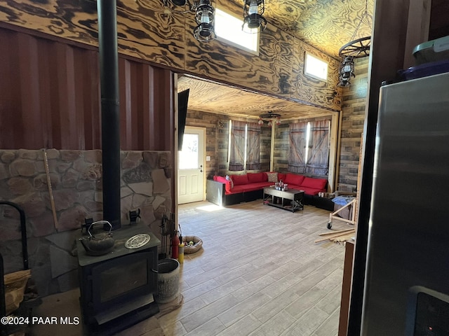 interior space featuring a wood stove, wood walls, light hardwood / wood-style flooring, and a towering ceiling