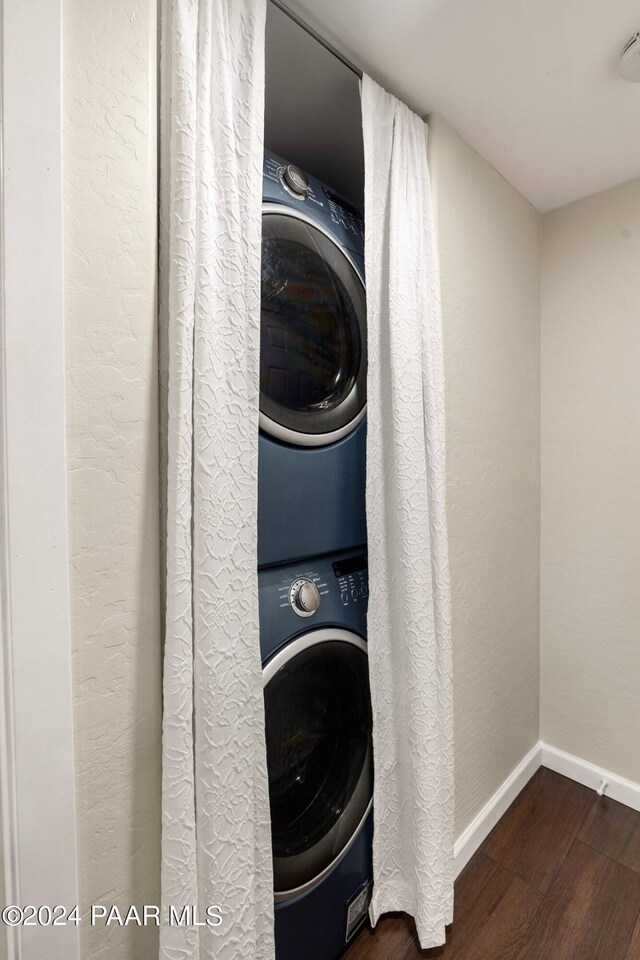 clothes washing area featuring dark wood finished floors, laundry area, baseboards, and stacked washer and clothes dryer