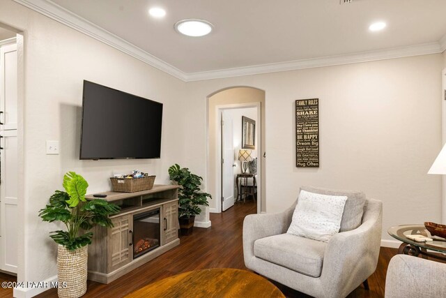 living area with a glass covered fireplace, crown molding, arched walkways, and dark wood-style flooring