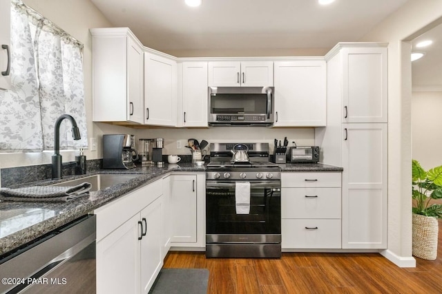 kitchen with dark stone counters, white cabinets, wood finished floors, and appliances with stainless steel finishes