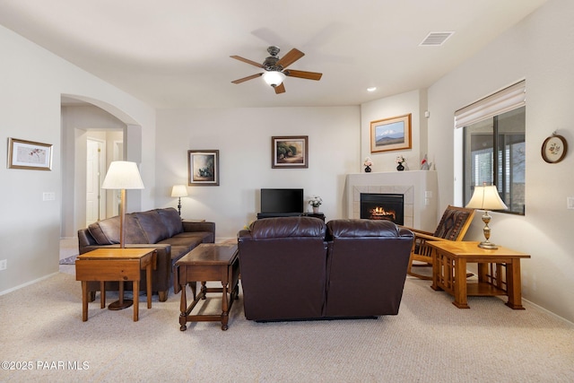 living area with visible vents, baseboards, arched walkways, a tiled fireplace, and light colored carpet