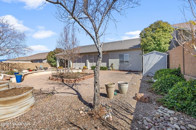 back of house featuring a patio, a fenced backyard, stucco siding, an outdoor structure, and a storage unit