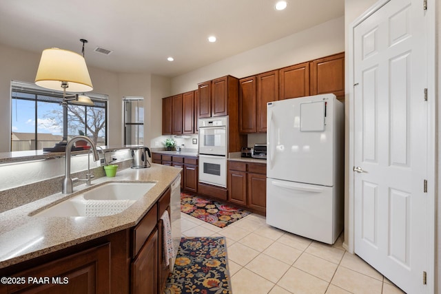 kitchen with visible vents, light tile patterned floors, hanging light fixtures, white appliances, and a sink