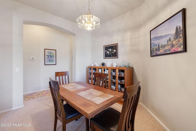 dining area with a notable chandelier, carpet flooring, arched walkways, and baseboards