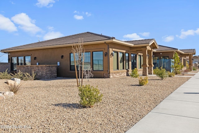 rear view of property with a tiled roof, stucco siding, stone siding, and fence