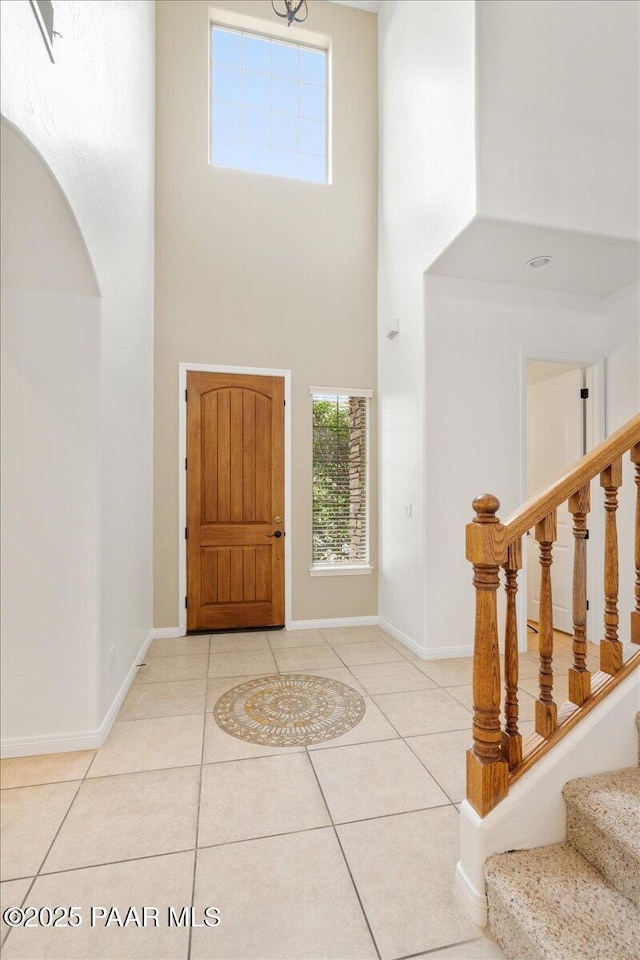 entrance foyer featuring light tile patterned floors, baseboards, arched walkways, stairs, and a towering ceiling