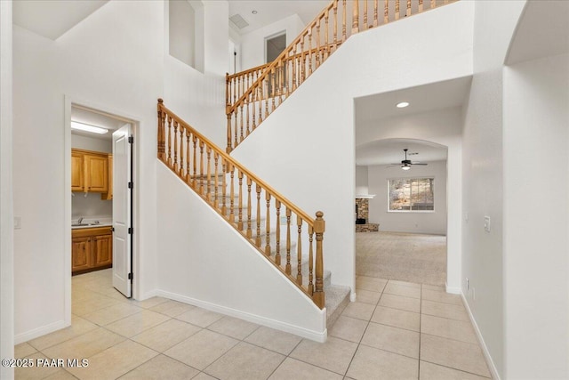 stairway featuring tile patterned floors, a ceiling fan, arched walkways, a high ceiling, and baseboards