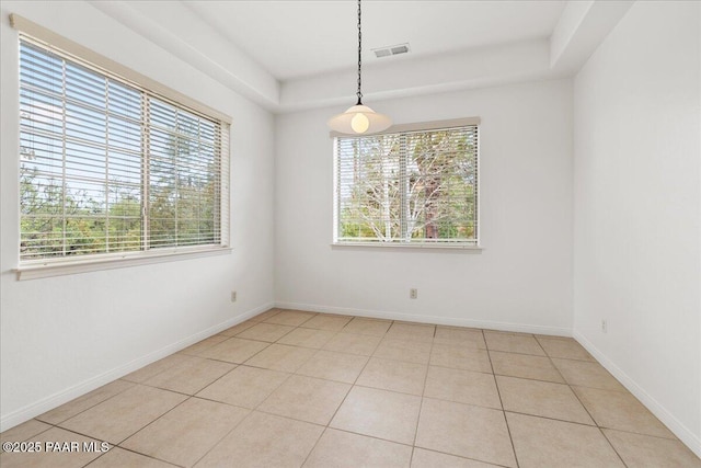 spare room featuring light tile patterned floors, visible vents, baseboards, and a tray ceiling