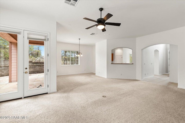 unfurnished living room with visible vents, carpet floors, arched walkways, and a ceiling fan