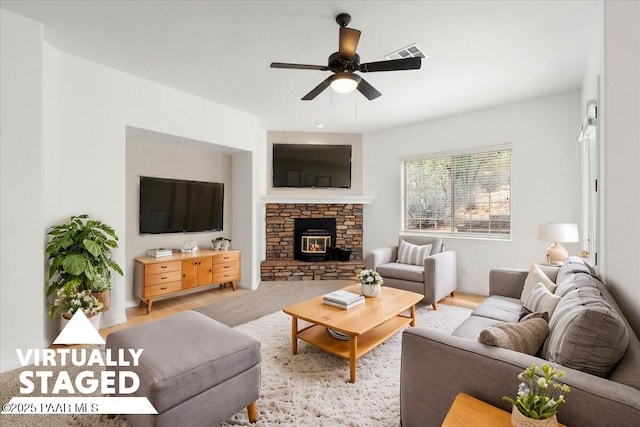 living area featuring a stone fireplace, a ceiling fan, and visible vents