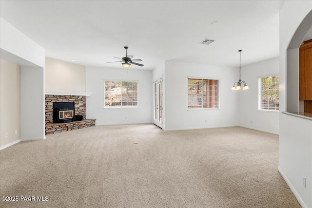 unfurnished living room with visible vents, baseboards, light carpet, a stone fireplace, and ceiling fan with notable chandelier