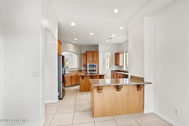 kitchen featuring a breakfast bar, stainless steel appliances, arched walkways, a peninsula, and light stone countertops