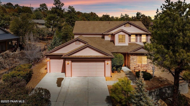 traditional-style house featuring stone siding, an attached garage, and concrete driveway