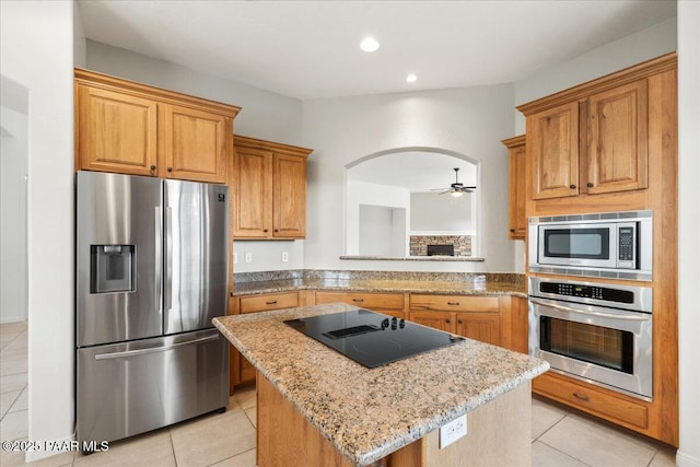 kitchen featuring a center island, stainless steel appliances, light tile patterned floors, light stone countertops, and ceiling fan