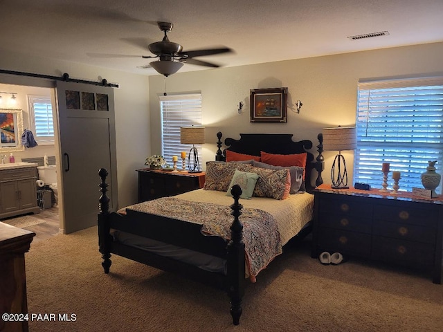 bedroom featuring a barn door, ensuite bathroom, ceiling fan, and light colored carpet