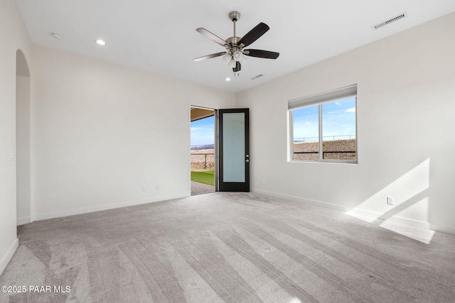 unfurnished room with carpet flooring, visible vents, baseboards, a ceiling fan, and arched walkways