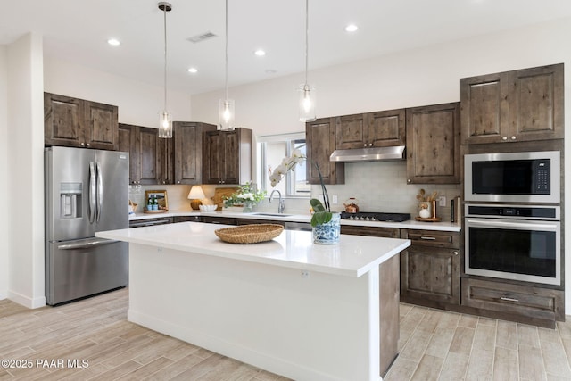 kitchen with backsplash, stainless steel appliances, under cabinet range hood, and visible vents