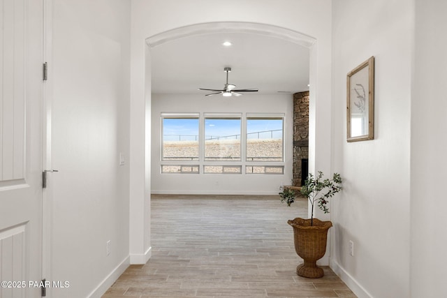 hall featuring light wood-style flooring, baseboards, and arched walkways