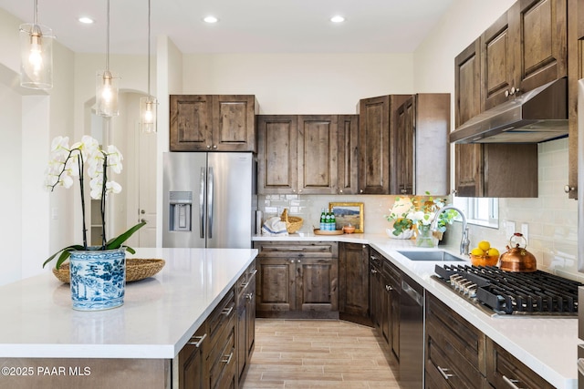 kitchen with light countertops, a center island, under cabinet range hood, a sink, and appliances with stainless steel finishes