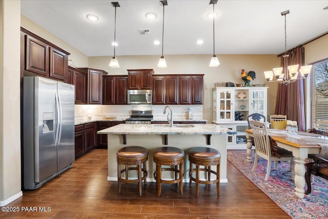 kitchen with pendant lighting, stainless steel appliances, tasteful backsplash, a kitchen island with sink, and a breakfast bar area