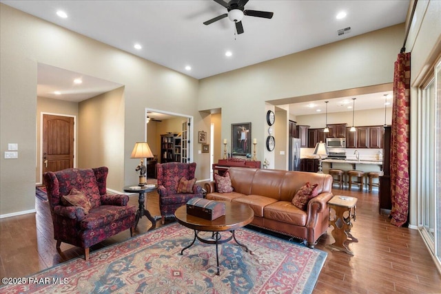 living room featuring ceiling fan, sink, wood-type flooring, and a high ceiling