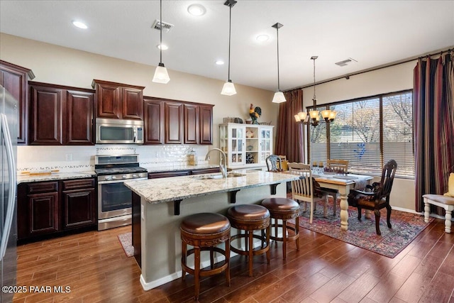 kitchen featuring hanging light fixtures, appliances with stainless steel finishes, sink, an island with sink, and decorative backsplash