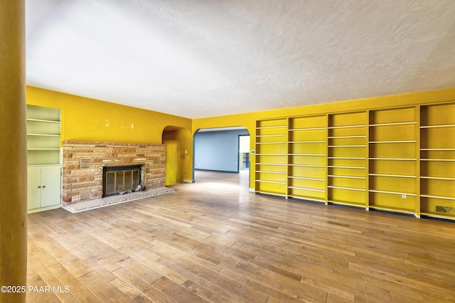 769 Cherokee Rd, Prescott, AZ 86303 - unfurnished living room featuring arched walkways, wood finished floors, a glass covered fireplace, a textured ceiling, and built in shelves