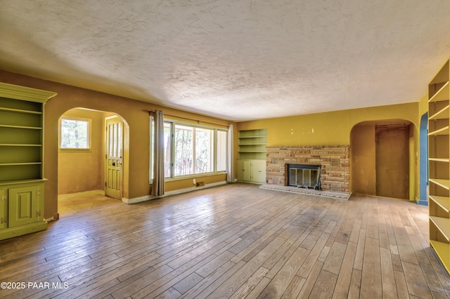 769 Cherokee Rd, Prescott, AZ 86303 - unfurnished living room with arched walkways, plenty of natural light, hardwood / wood-style floors, a brick fireplace, and a textured ceiling